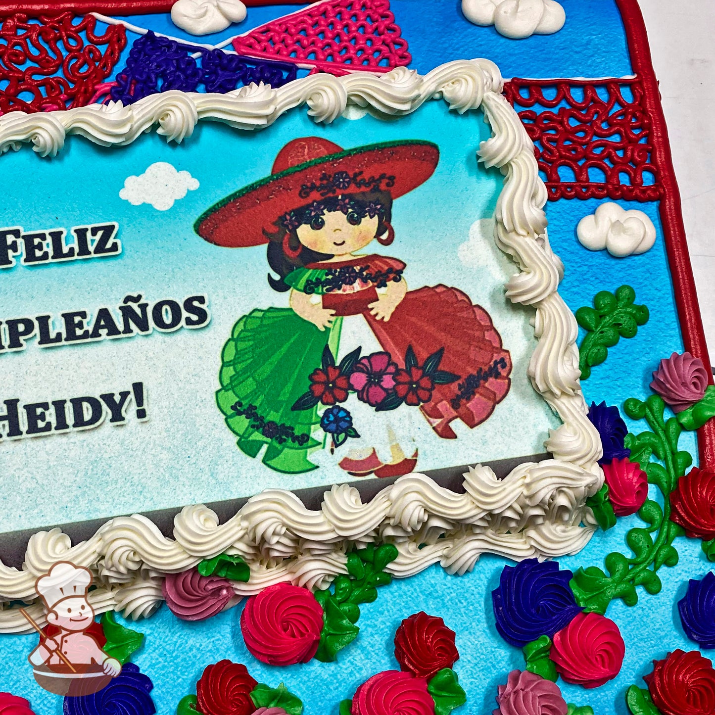 Sheet cake with colorful buttercream decorations, featuring a Mexican paper picado banner design. Red, pink, and purple swirled flowers with green leaves.