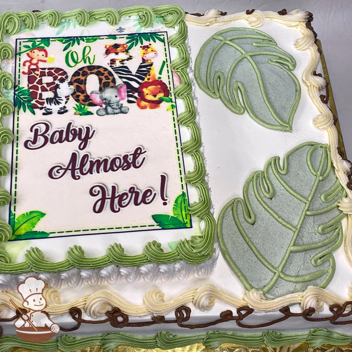 Sheet cake with green buttercream border, Monstera leaves piped on the right, and a printed photo layer on the left. Cream and brown swirls on the edges.