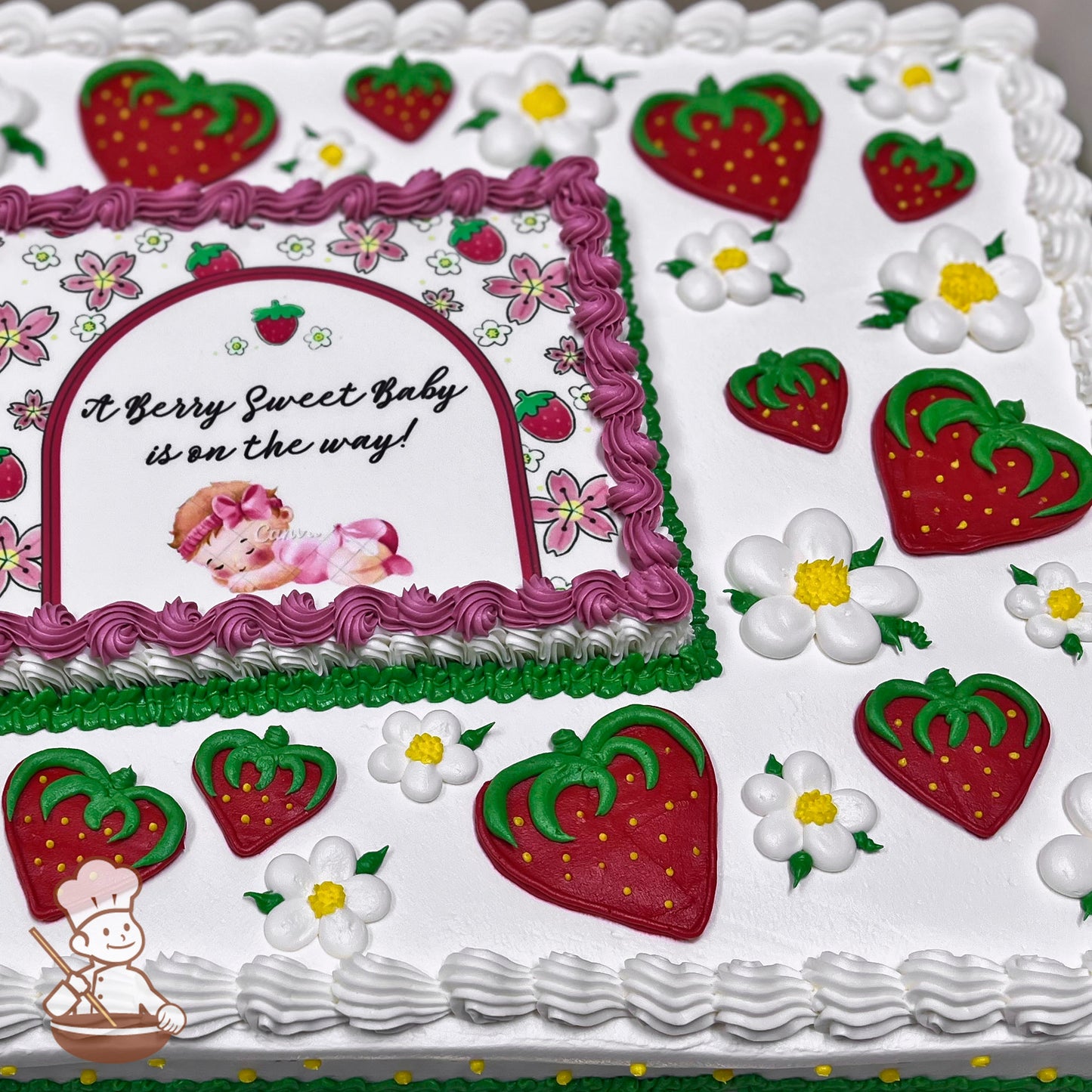 Sheet cake with white frosting, decorated with red strawberries, white daisies with yellow centers, and green leaves. Pink and green borders accent the design.
