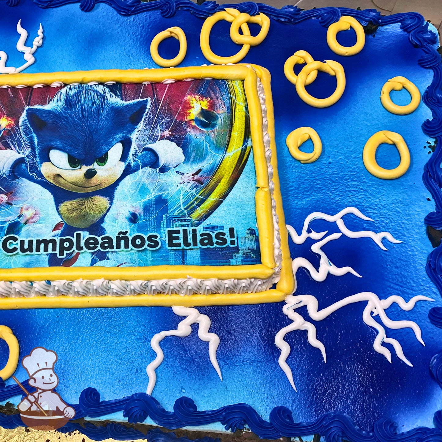 Sheet cake with a blue background, decorated with gold rings and white lightning designs. The edges have blue piping, and a printed image is framed in yellow.