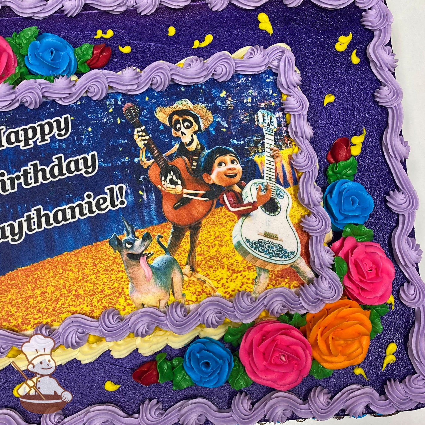 Purple sheet cake with colorful buttercream roses in pink, blue, and orange at the corners. Yellow accents and a printed image in the center.