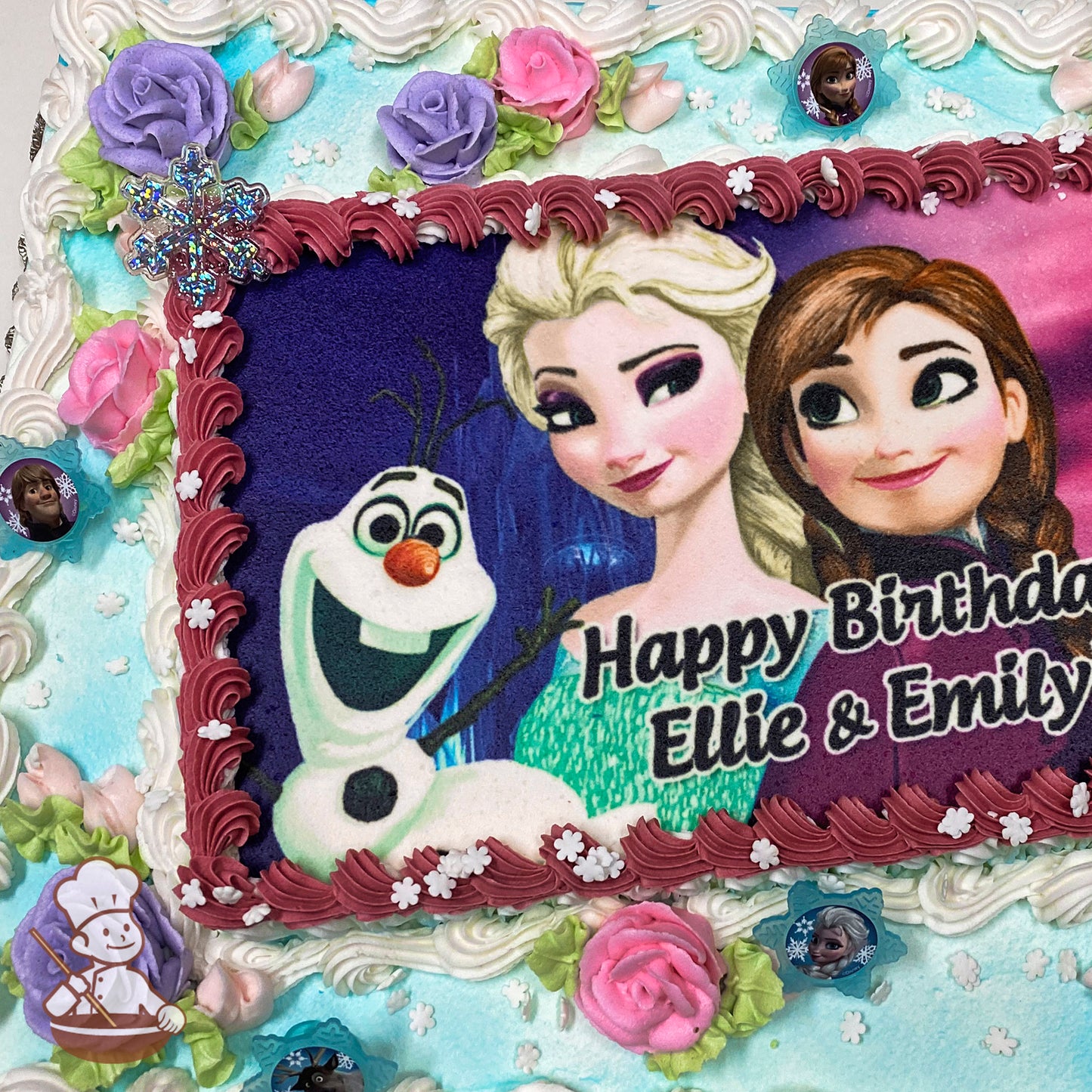 Sheet cake with a Frozen theme, featuring buttercream roses in pink, purple, and green, plastic snowflake decorations, and Frozen-themed plastic rings.