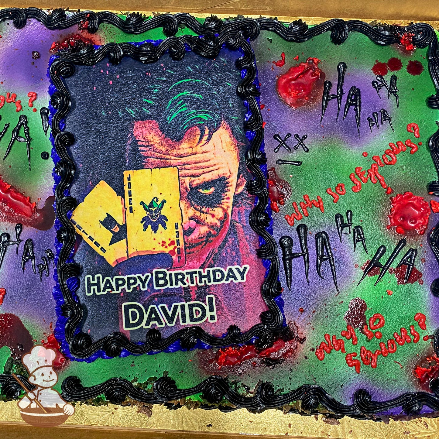 A rectangular sheet cake with a printed photo layer bordered by black buttercream. The background is airbrushed in green and purple with red gel resembling blood splatters. Black and red text and symbols, including "HA HA" and "Why so serious?", are scattered across the surface.