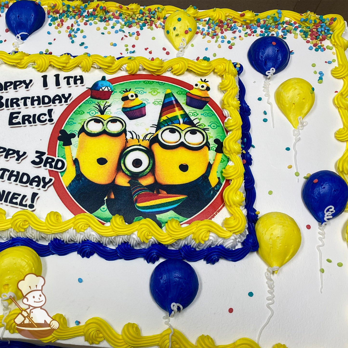 Sheet cake with yellow and blue buttercream borders, buttercream yellow and blue balloon decorations, and colorful sprinkles scattered on white frosting.