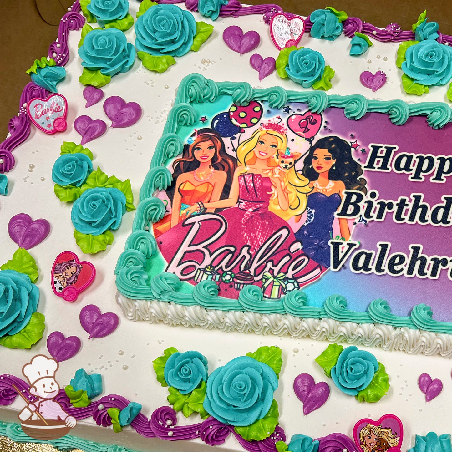 Sheet cake with aqua blue buttercream roses, green leaves, purple hearts, and Barbie-themed plastic rings as decorations. Purple and aqua borders.