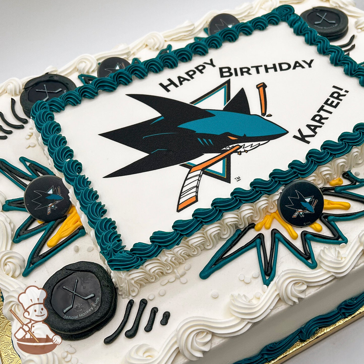 Sheet cake with teal and white buttercream borders, San Jose Sharks logo-themed plastic hockey puck decorations, and teal and yellow starburst designs.