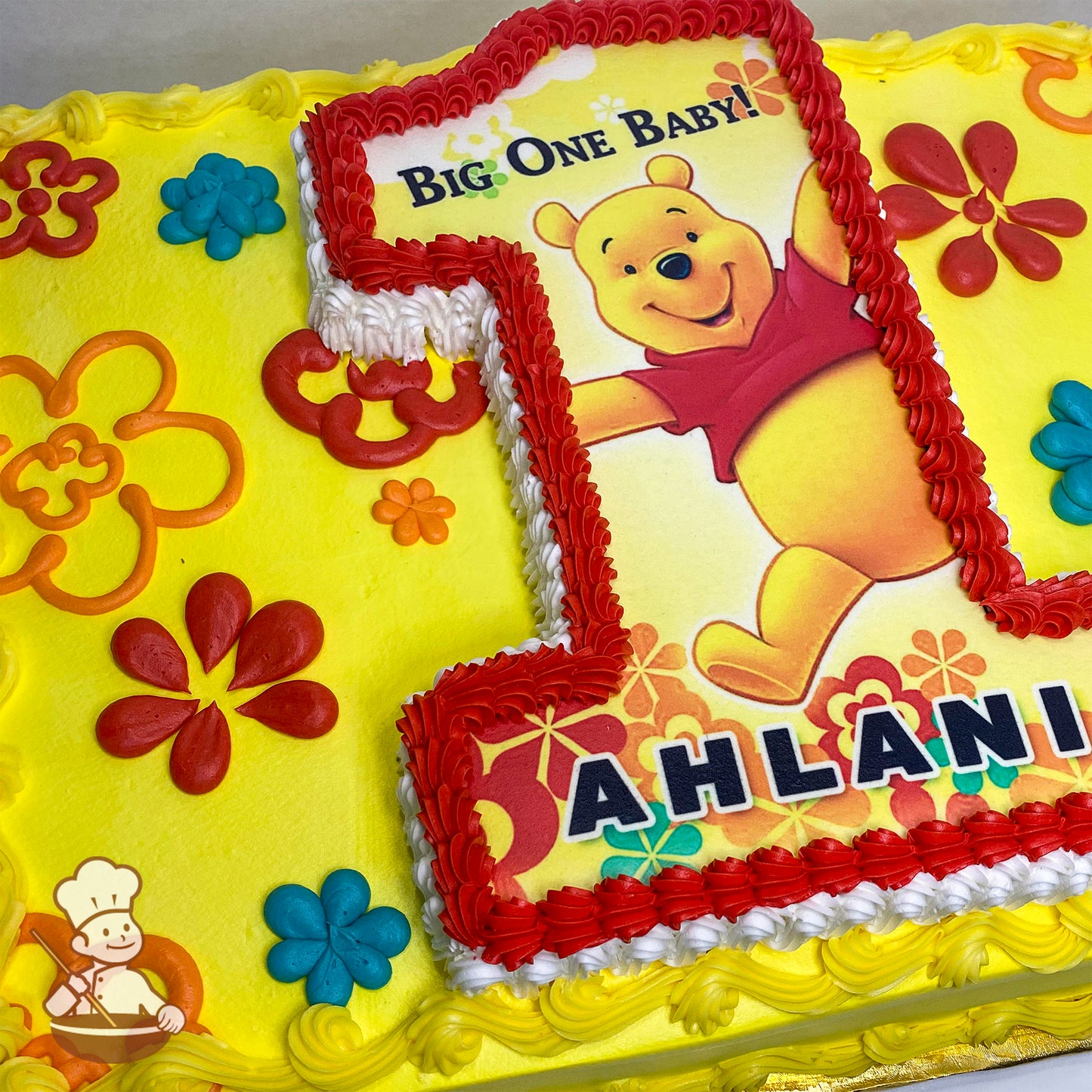 Yellow sheet cake with colorful buttercream flowers, featuring a red-bordered number 1 cutout of Winnie the Pooh in a red shirt, surrounded by floral designs.