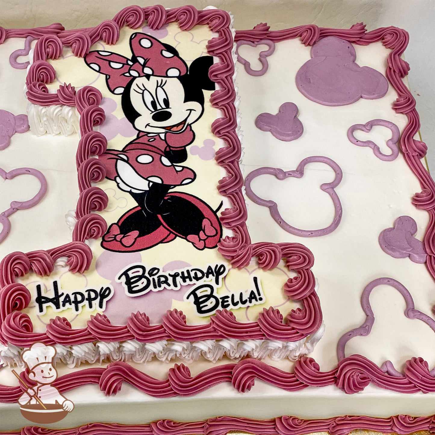 Sheet cake with buttercream decorations, featuring Minnie Mouse in a pink polka-dot outfit on a number "1" cutout. Pink Mickey-shaped patterns border the cake.