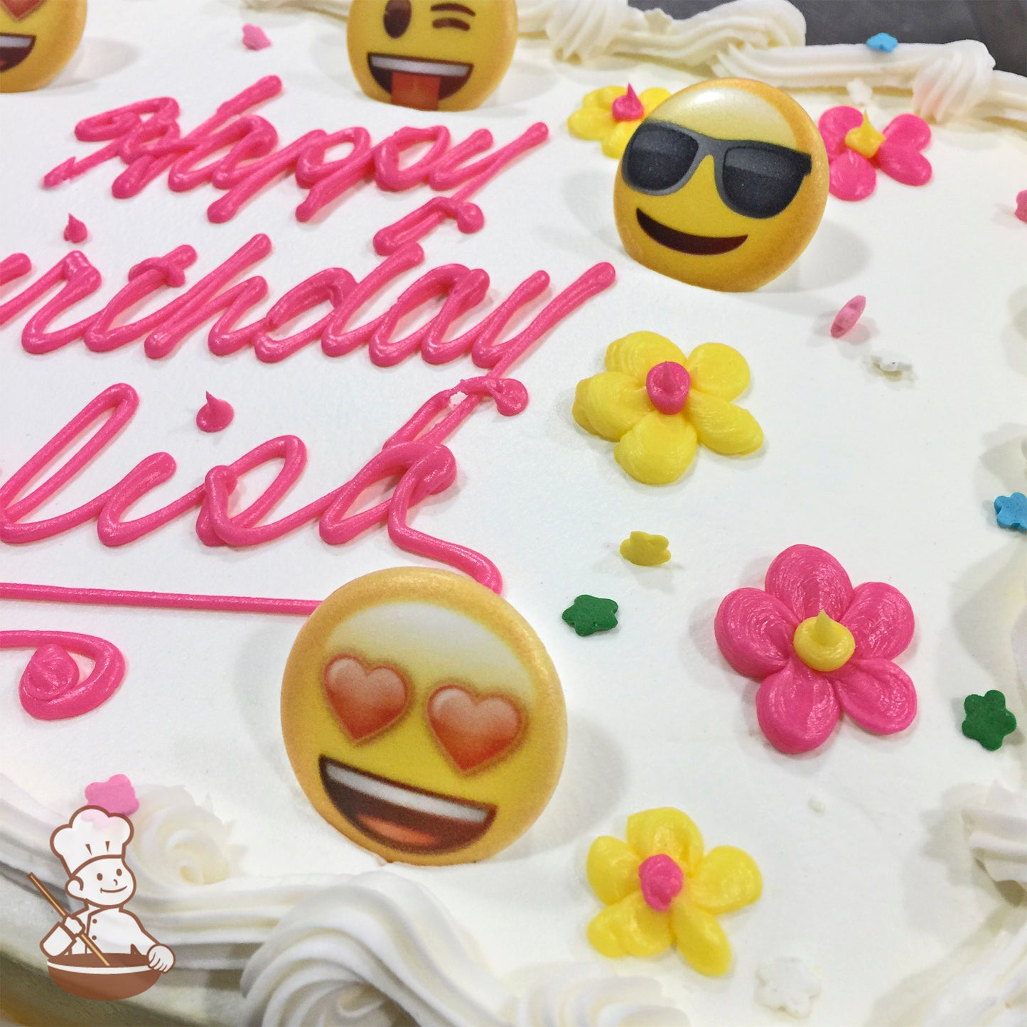 Sheet cake with emoji rings and colorful buttercream flowers. Emojis include heart eyes, sunglasses, and winking faces. Pink and yellow flowers.