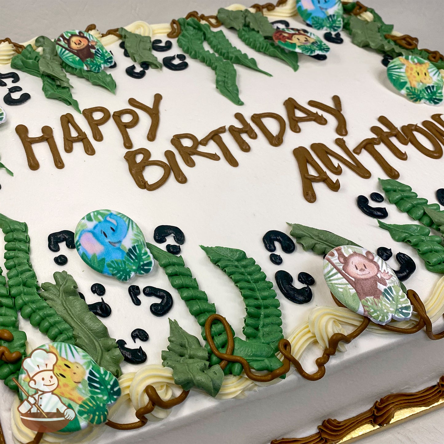 Sheet cake with white frosting, decorated with green buttercream jungle leaves, plastic rings featuring safari animals (elephant, giraffe, monkey), and animal print accents.