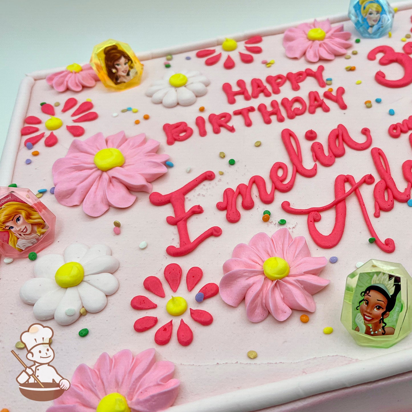 A pink sheet cake decorated with buttercream daisies in pink and white, colorful sprinkles, and plastic Disney Princess rings featuring various characters.