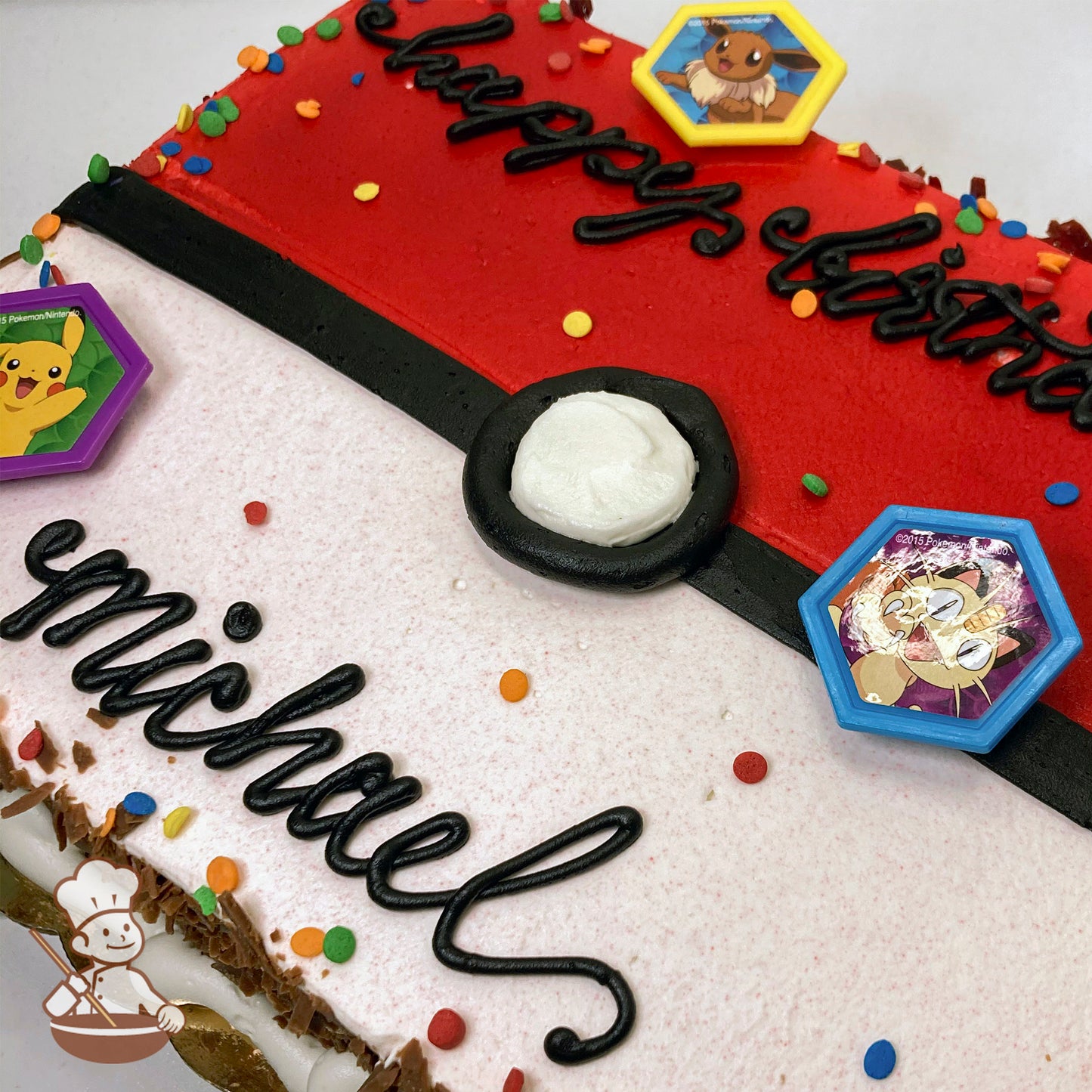 Sheet cake decorated as a Pokéball with red and white buttercream, black icing details, colorful sprinkles, and plastic Pokémon rings featuring Pikachu, Eevee, and Meowth.