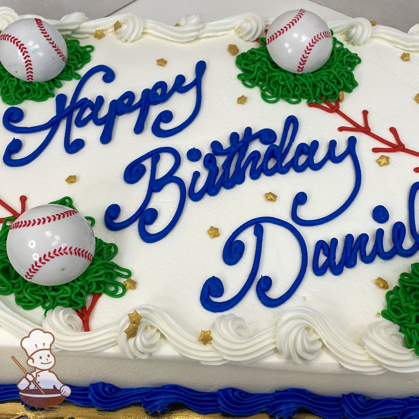 Sheet cake with white frosting, plastic baseball decorations on green icing grass patches, gold star sprinkles, and blue icing border.