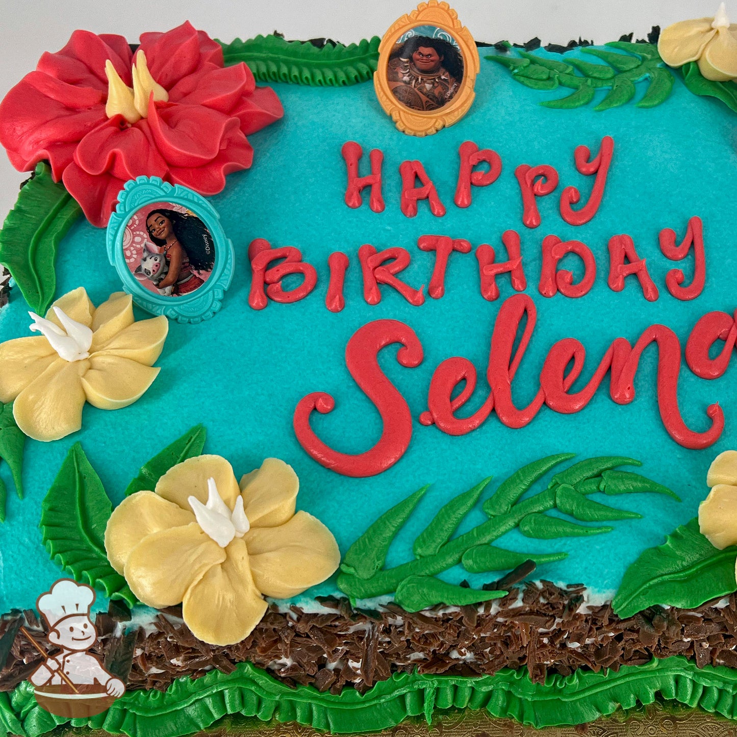 Sheet cake with blue canvas, light red and yellow hibiscus flowers, green leaf accents, and Moana-themed plastic rings.