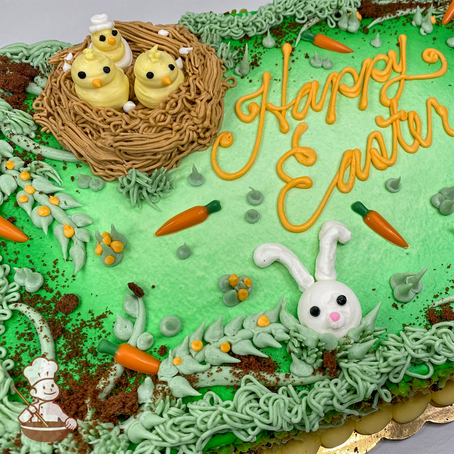 Sheet cake with green frosting, a buttercream nest holding three yellow chicks, a white bunny face, orange chocolate carrots, and cake crumb "dirt."