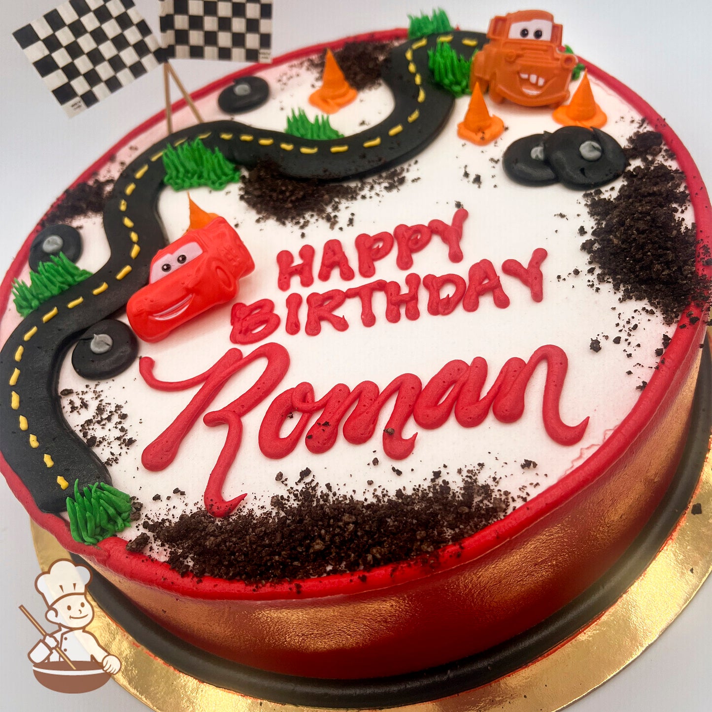 Round cake with a Cars theme, featuring a black icing road, Lightning McQueen and Mater plastic rings, cake crumb "dirt," and green grass accents.