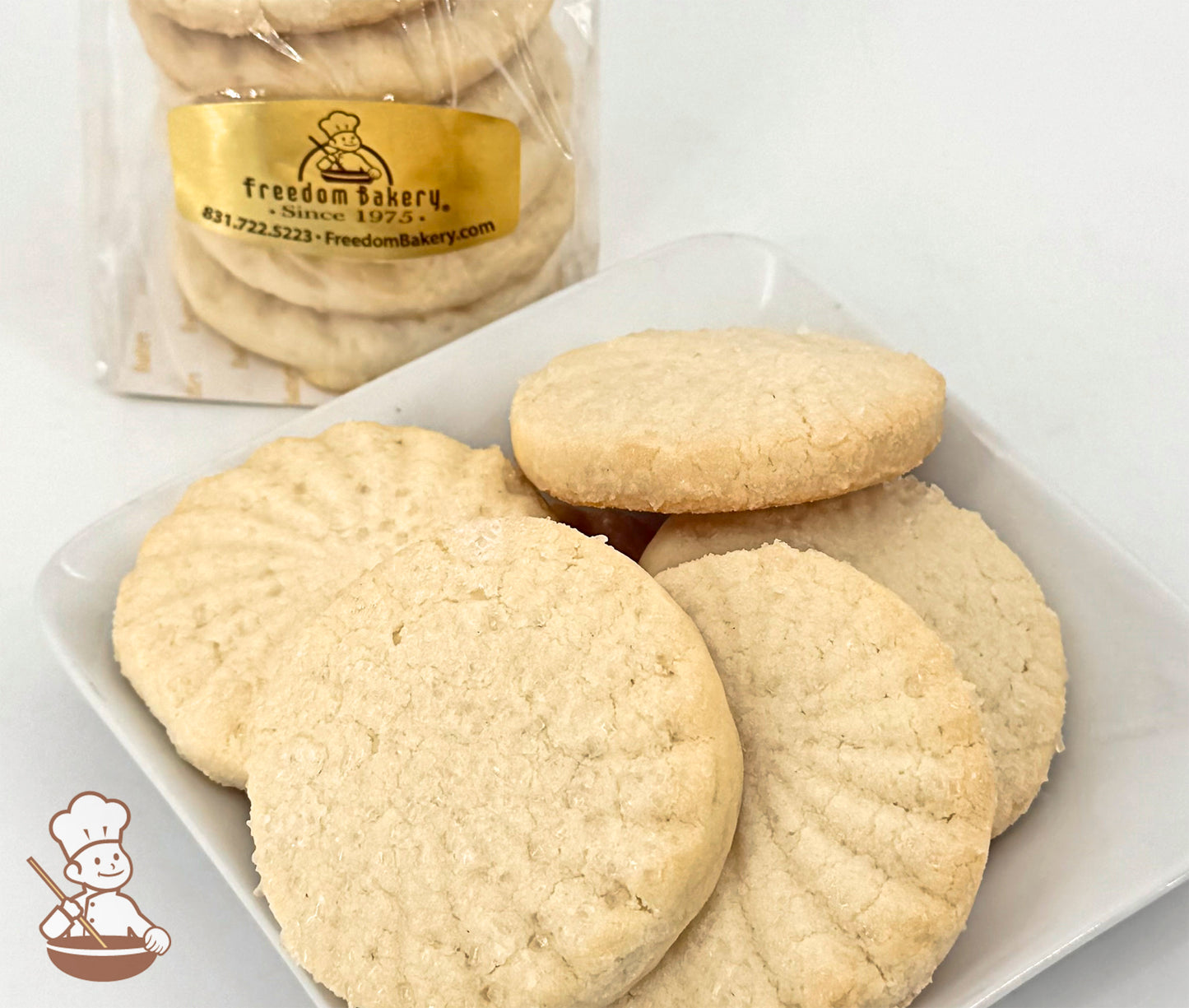 Six butter shortbread cookies on a white plate, with a bag of similar cookies in the background.