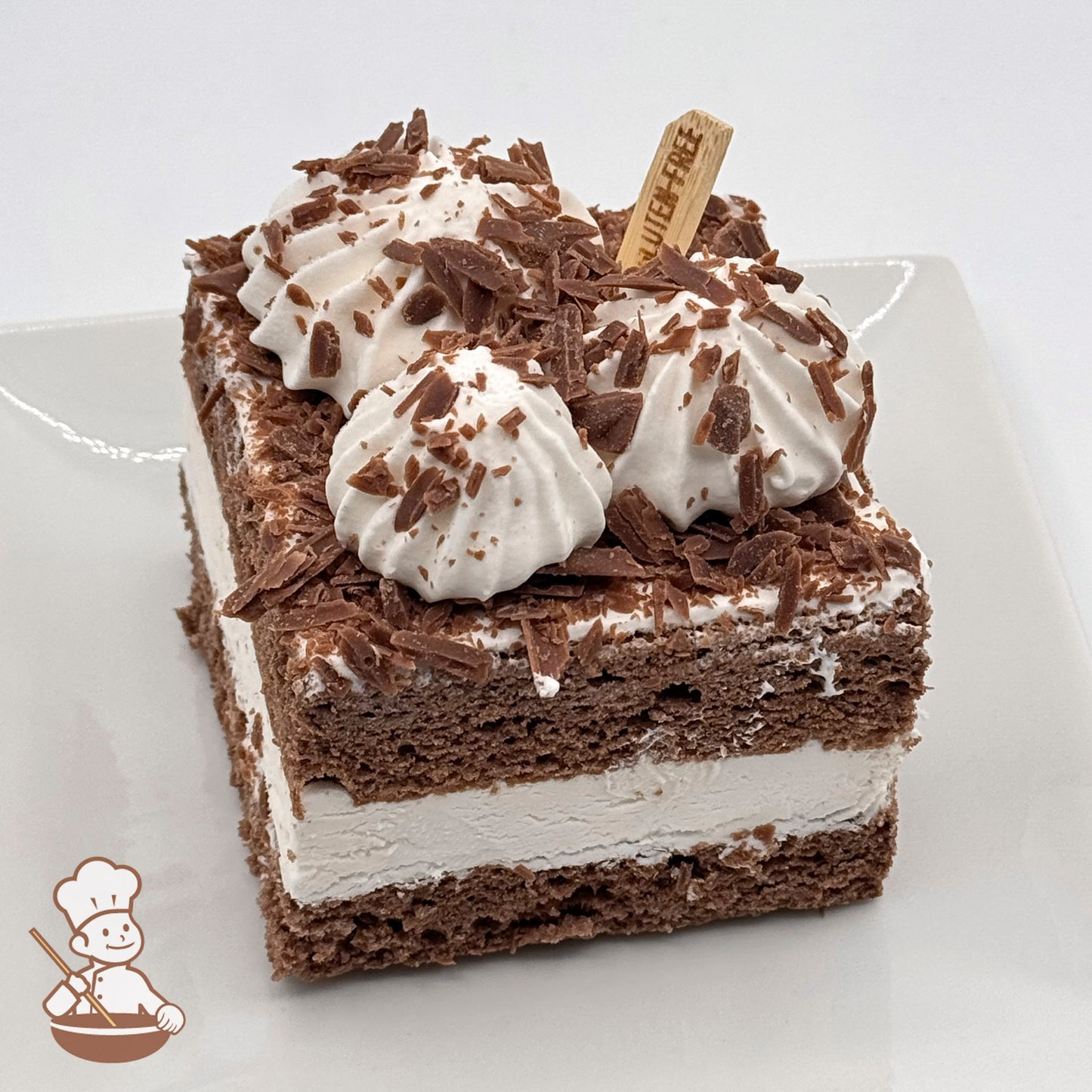 A slice of gluten-free chocolate chiffon cake topped with whipped cream and chocolate shavings on a white plate.