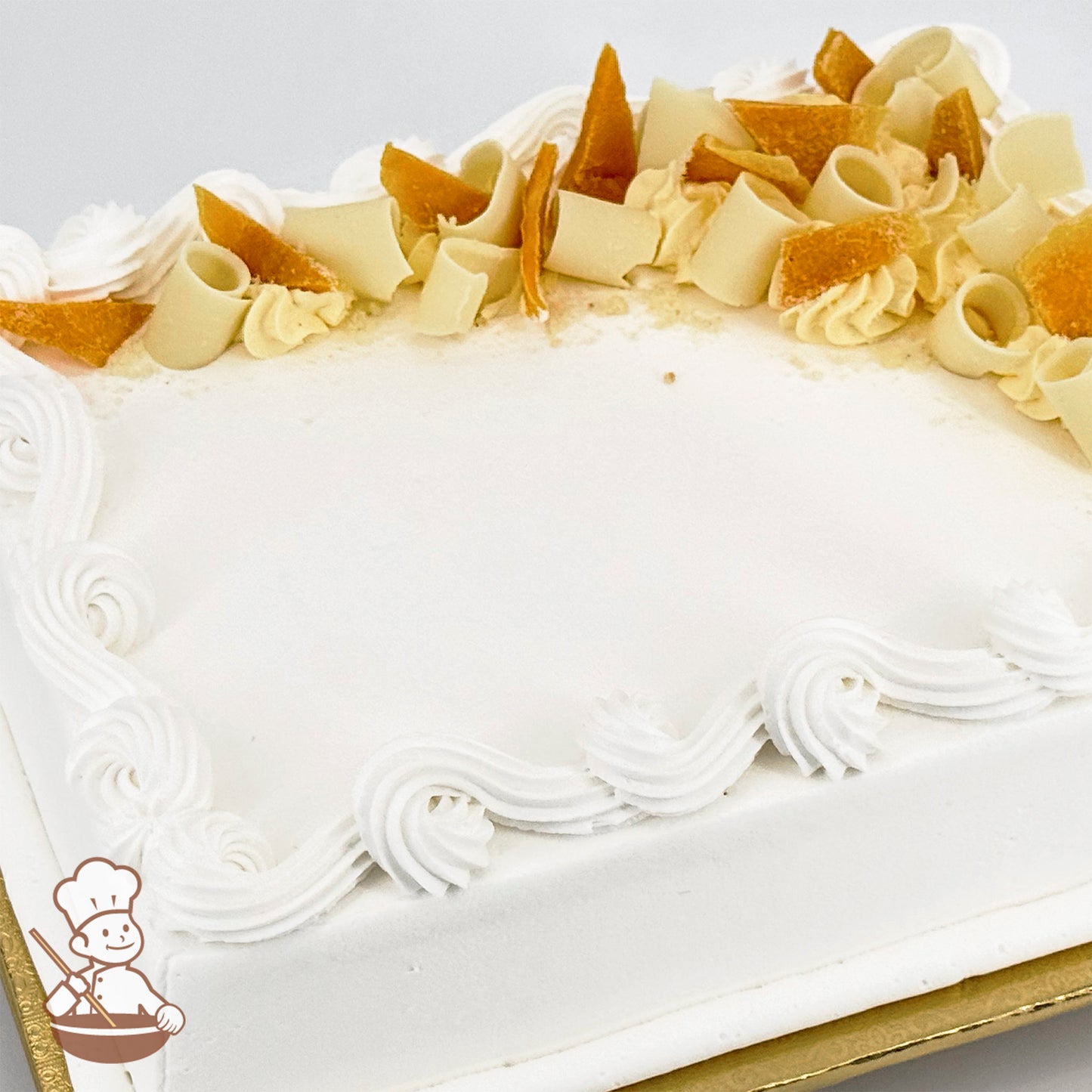 White sheet cake with swirled trim topped with white chocolate curls and dried mango peels.