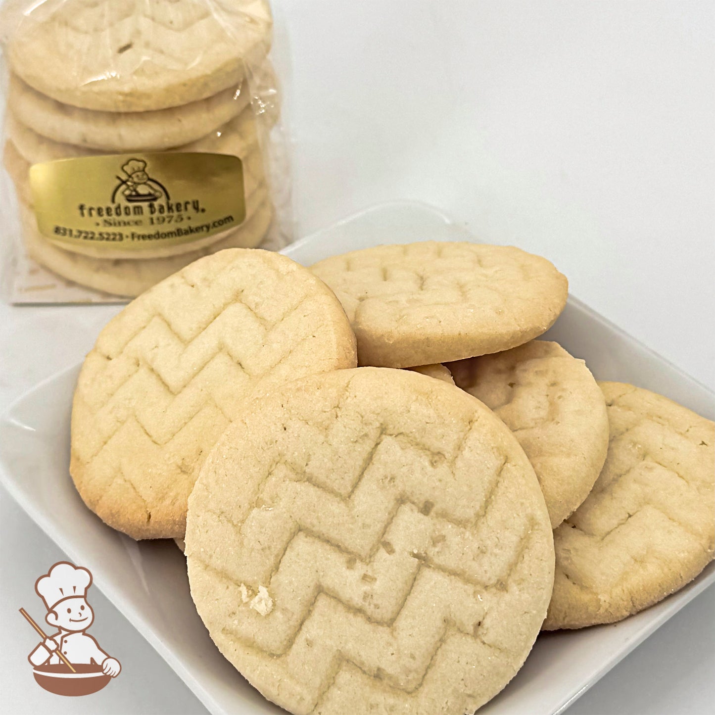 Six round shortbread cookies on a white plate. A bag of similar cookies is visible in the background.