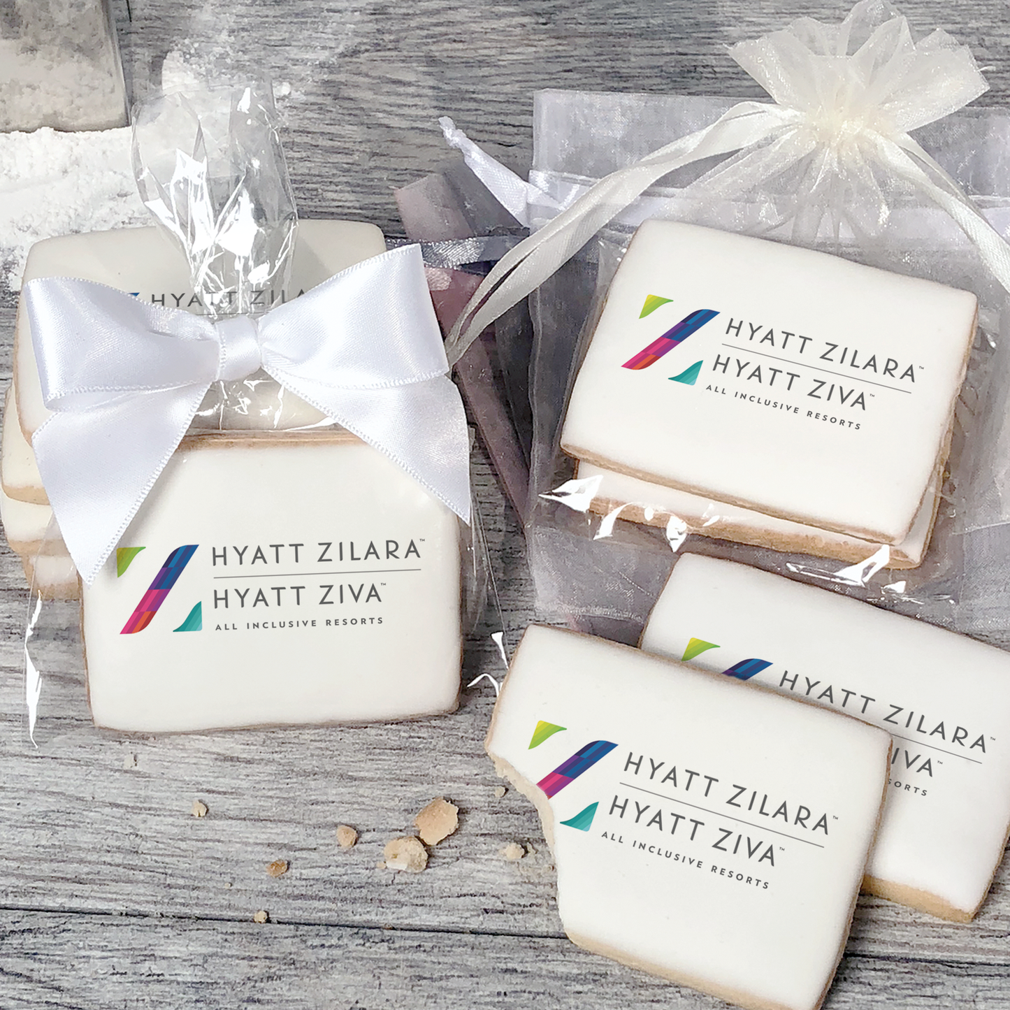 A stack of rectangular butter shortbread cookies with Hyatt Zilara logo printed directly on a white, light sugar icing. Some cookies are shown in clear packaging with a twist-tie ribbon bow or inside an organza bag.