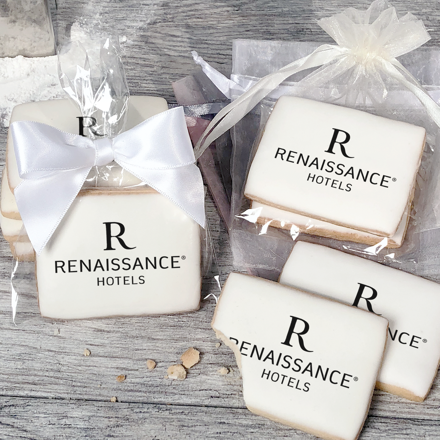 A stack of rectangular butter shortbread cookies with Renaissance logo printed directly on a white, light sugar icing. Some cookies are shown in clear packaging with a twist-tie ribbon bow or inside an organza bag.