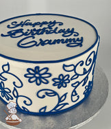 Single tier cake with white icing, and decorated with blue buttercream scrolls.