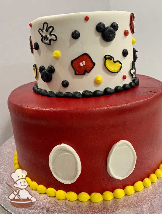 2-tier cake with red icing on the bottom tier and two white circles to look like Mickey's pants. The top tier has buttercream Mickey decorations.