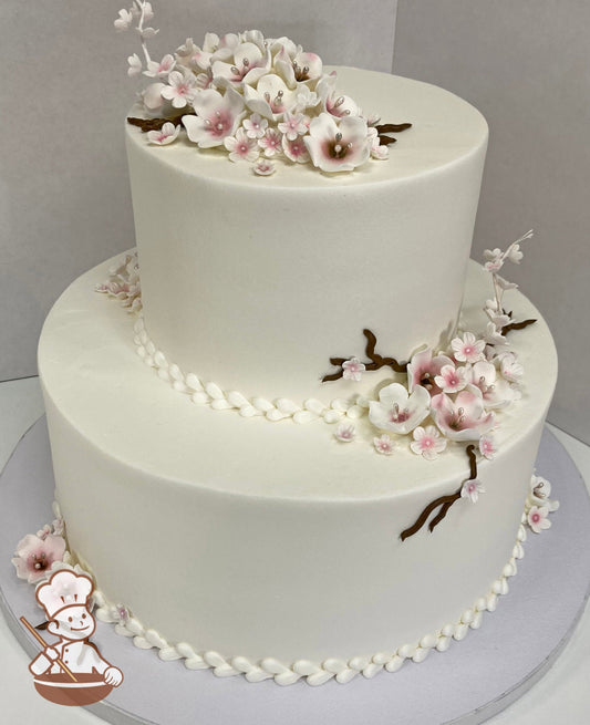 2-tier cake with smooth white icing and decorated with white and pink sugar cherry blossom flowers and brown buttercream branches.