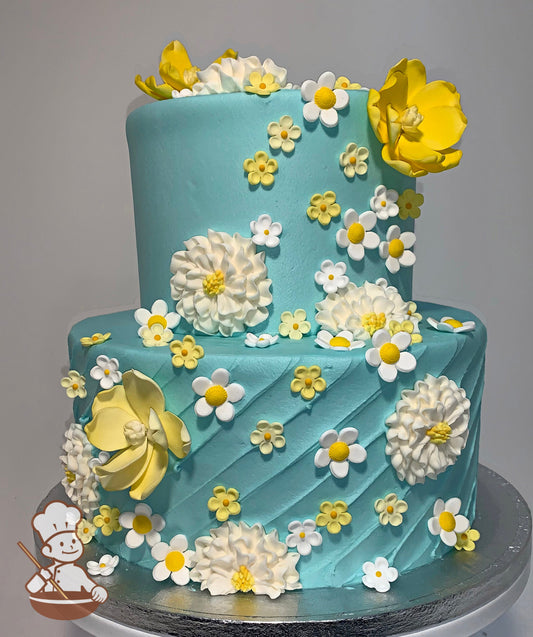 2-tier cake with light blue icing, decorated with a vertical stripe texture on the bottom tier and yellow and white sugar flowers all over.