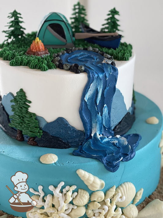 2-tier cake decorated with seashells, "sand", buttercream mountains, buttercream trees, buttercream waterfall and a camping toy.