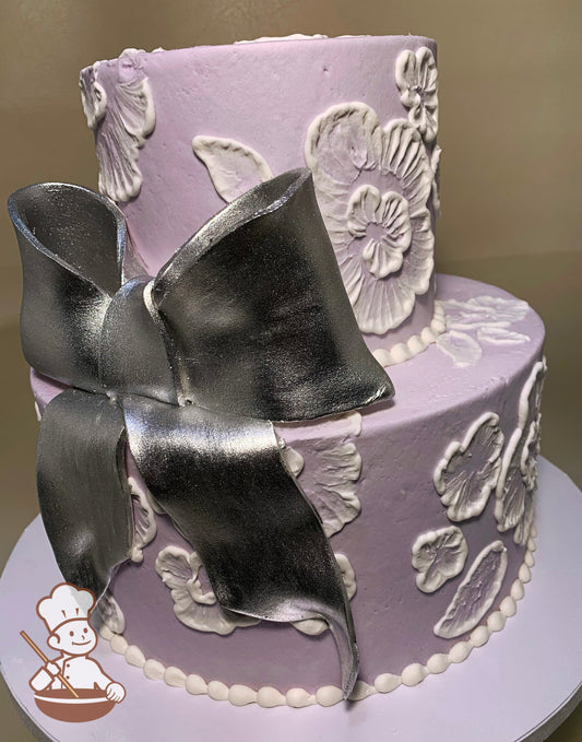 2-tier cake with smooth lavender icing and decorated with white buttercream lace florals and a big silver fondant bow.