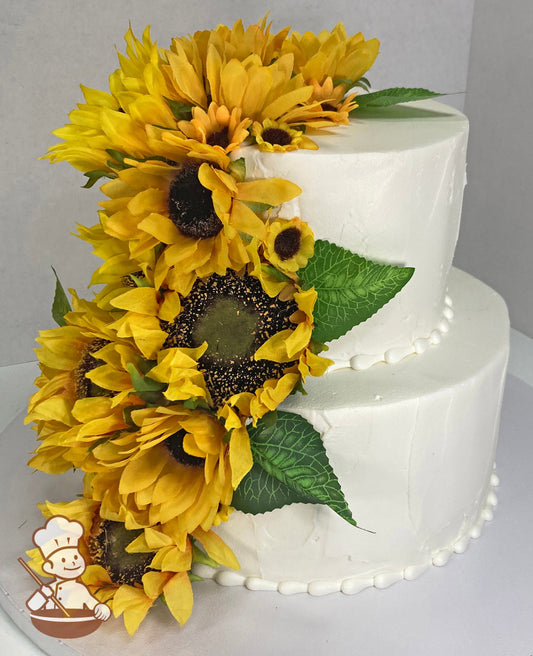 2-tier cake with white icing and decorated with a light texture and silk sunflowers cascading on the tiers.