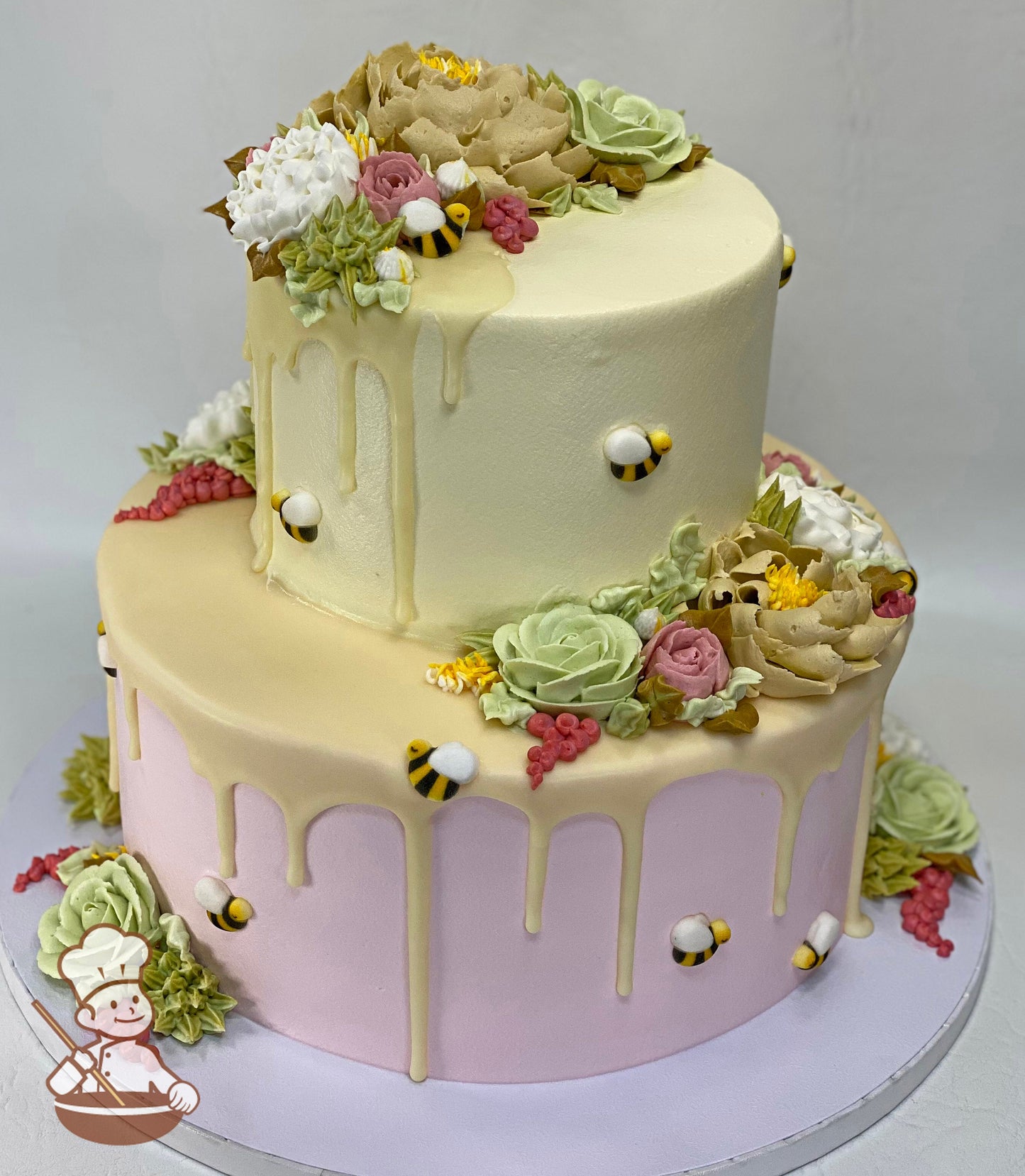 Cake decorated with pink icing on the bottom tier and yellow icing on the top tier. The cake also has buttercream flowers, bees and yellow drip.