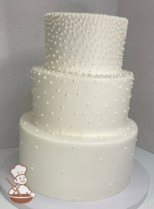 3-tier round cake with smooth white icing and white buttercream dots mostly on the top tier and less dots as you go down the cake.