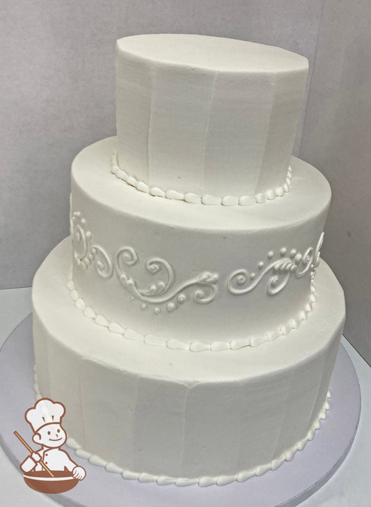 3-tier round cake with white icing and the top and bottom tier have a vertical textured icing and the middle tier has white buttercream scrolls.