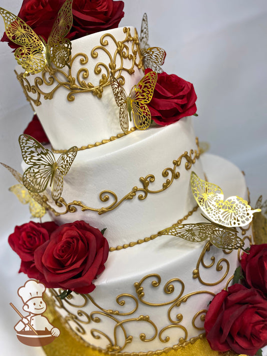3-tier round cake with smooth white icing on all the tiers and decorated with metallic gold scrolls, gold butterflies and silk red roses.