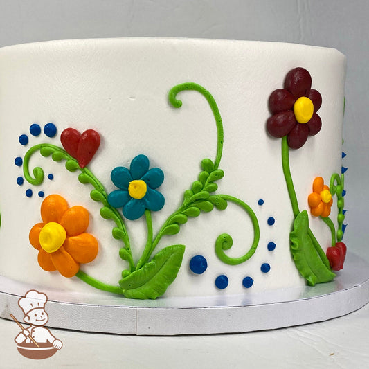Round cake with white icing with colorful buttercream daisies, leaves and dots around the sides.