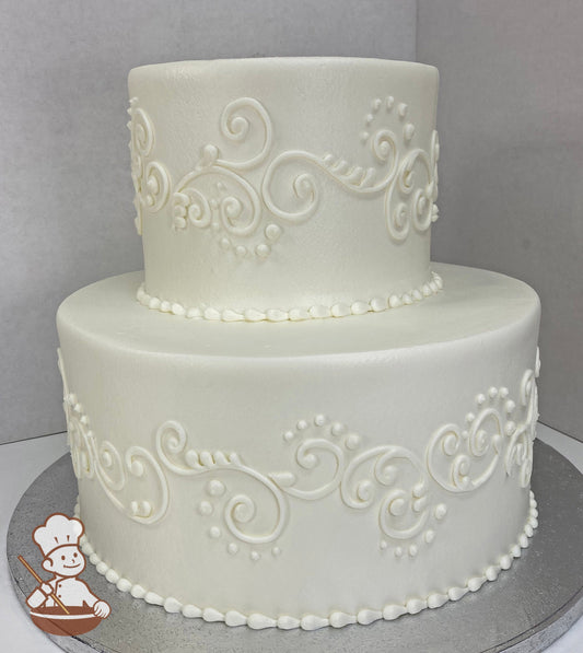 Two-tier round cake with white icing, decorated with white buttercream scrolls and white beaded trims on both tiers.