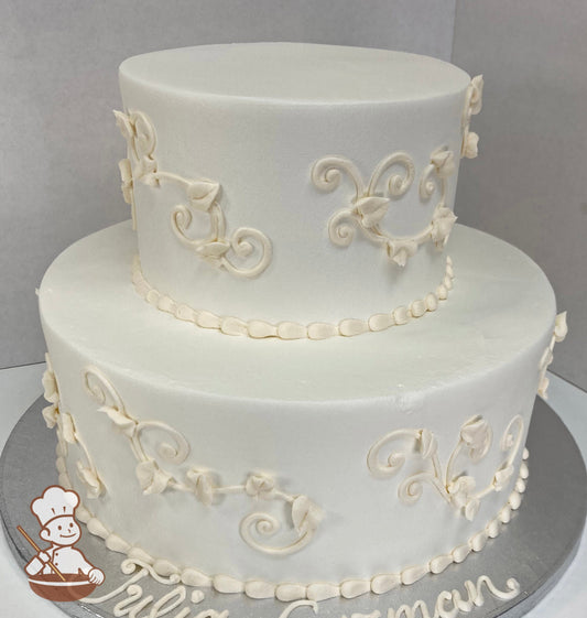 2-tier round cake with white icing, decorated with ivory-colored buttercream scrolls on cake walls with a beaded trim.