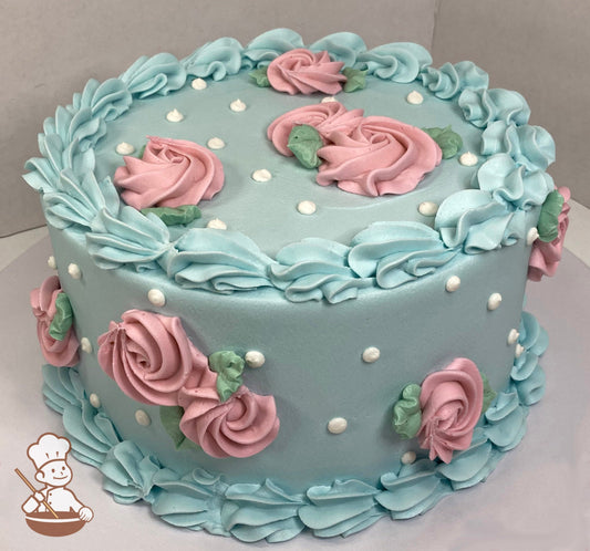 Single-tier round cake with smooth light blue icing and large shell trims on top and bottom of cake with light pink swirlettes and white dots.