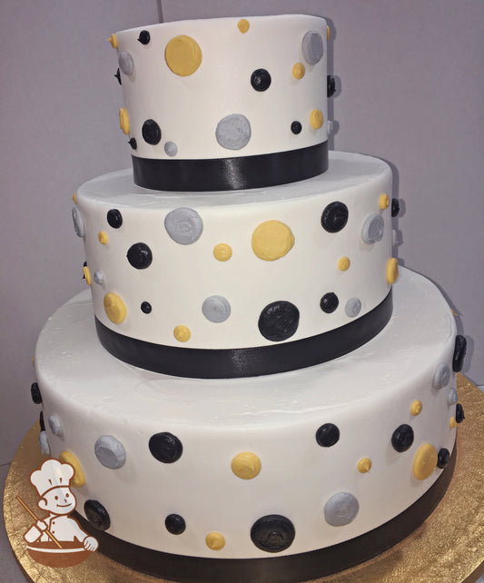 3-tier round cake with white icing, decorated with black, yellow and gray dots on cake walls and a black ribbon on the bottom of the tiers.