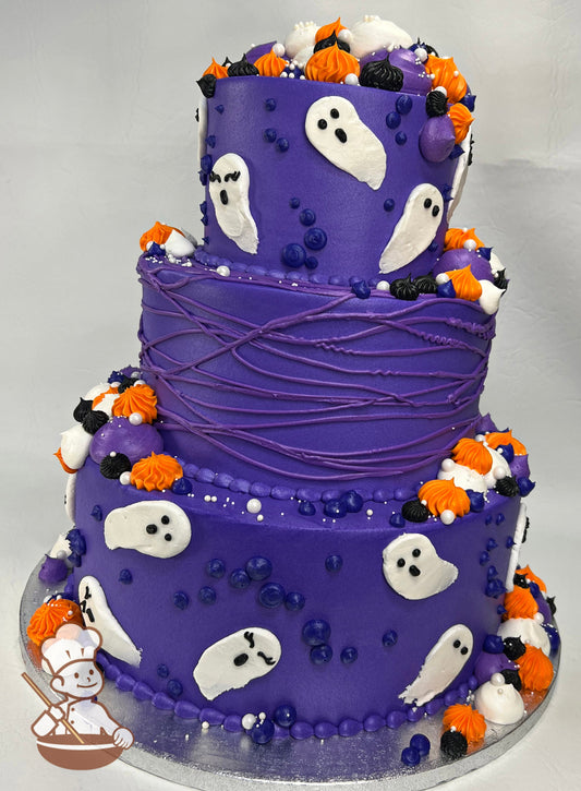 3-tier round cake with purple icing and white ghost decorations and other festive Halloween themed decorations in Halloween colors on all tiers.