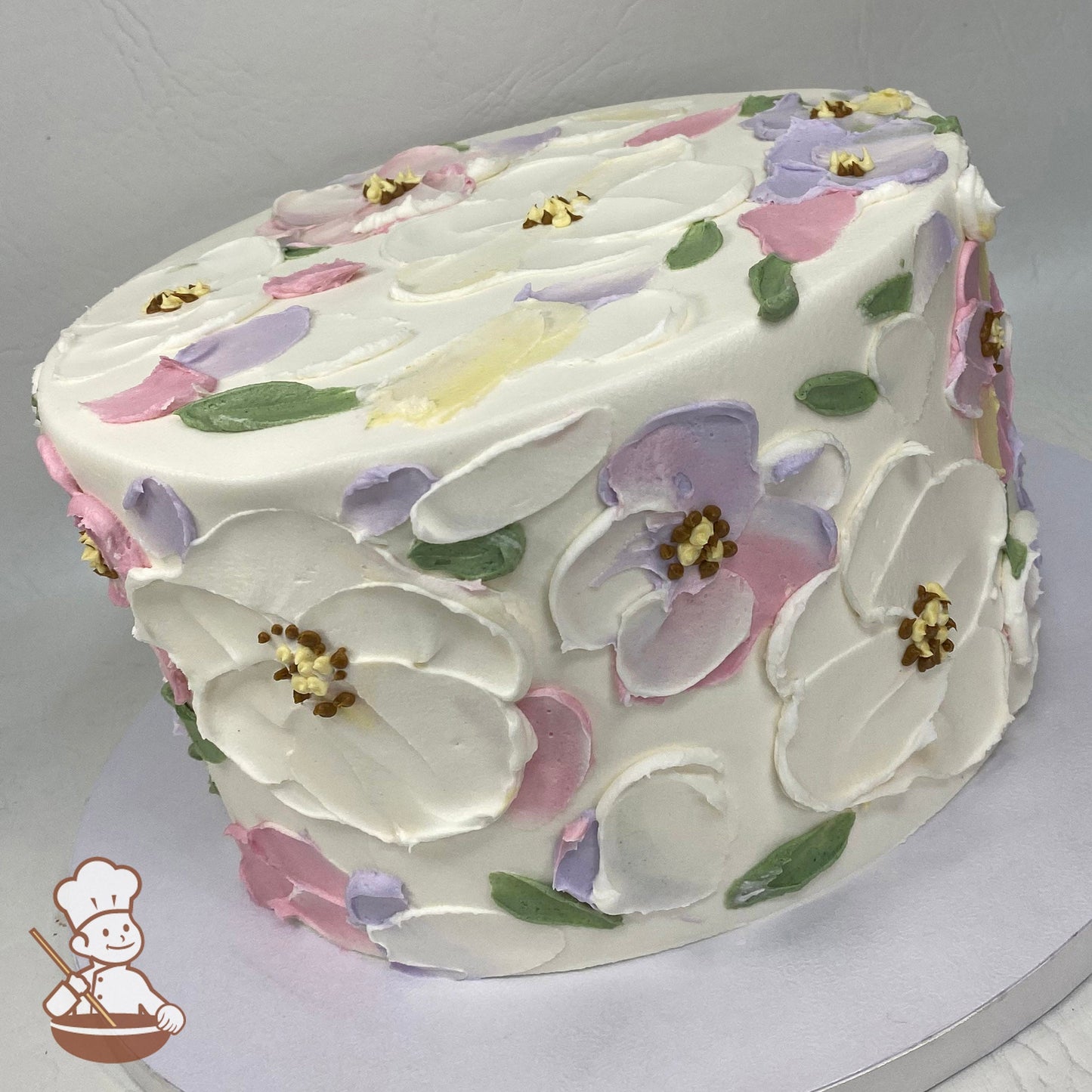Single tier cake with smooth white icing, decorated with lavender, mauve and white palette knife flowers.