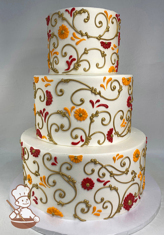 3-tier cake with smooth white icing, decorated with hand-piped gold scrolls and buttercream daisies in red and orange.