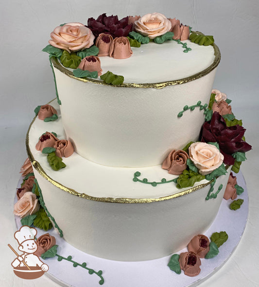 2-tier cake with smooth white icing, decorated with burgundy and light peach colored buttercream flowers and gold-painted trims.