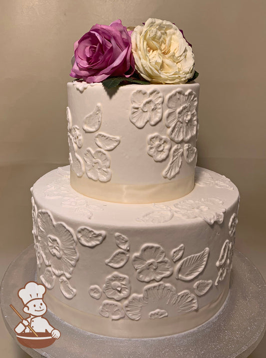 2-tier round cake with smooth white icing, decorated with white buttercream lace-like flowers and silk roses as topper on the cake.