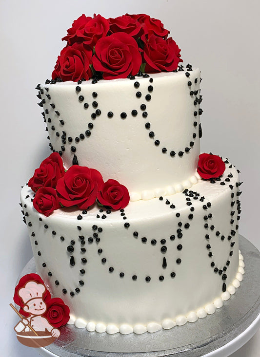 2 tier cake with smooth white icing, and decorated with red sugar roses and black buttercream dot loops.