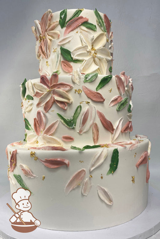 3-tier cake with smooth white icing, and decorated with buttercream palette knife flowers in peach-tones and ivory-tones and gold foil flakes.