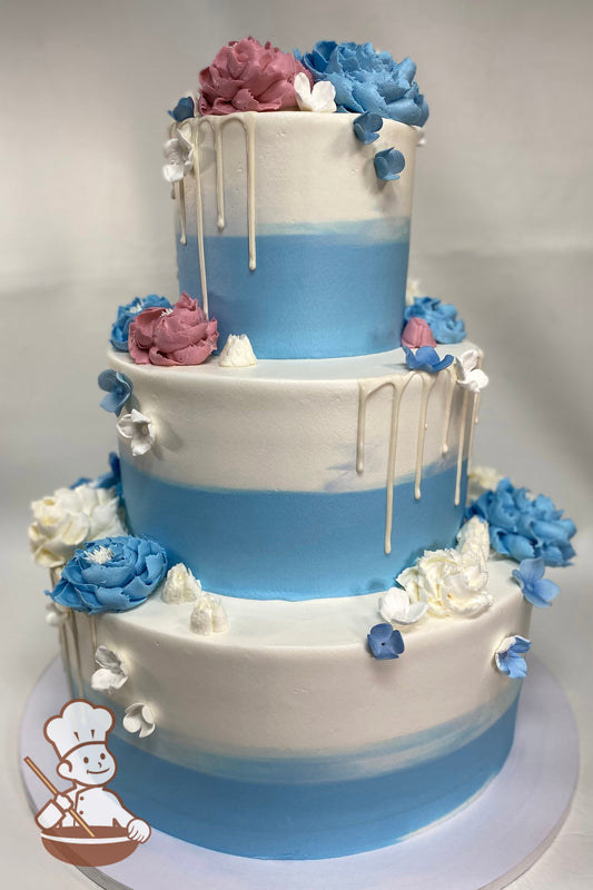 3-tier cake with white, blue and mauve colors, and decorated with large buttercream flowers and small sugar flowers and white drip.